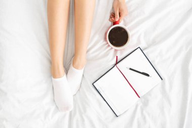 Kadın bacakları, dizüstü bilgisayarı ve yatakta bir fincan kahve.