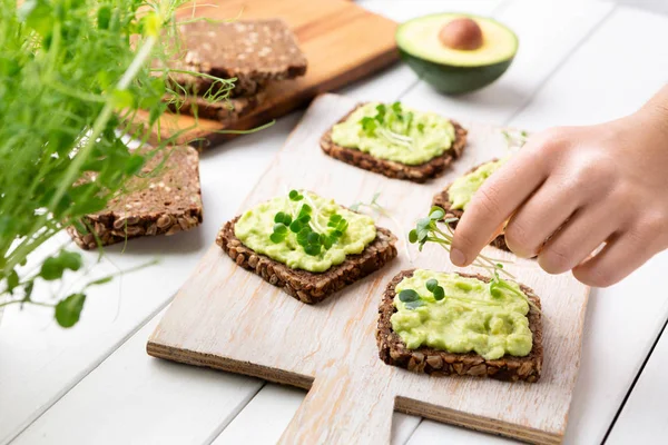 Woman preparing toasts with avocado spread and microgreens — Stock Photo, Image