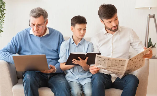 Мужская семья с помощью ноутбука, чтение книги и газеты на дому — стоковое фото
