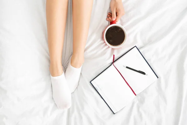 Вид сверху на женские ноги, ноутбук и чашку кофе в постели — стоковое фото