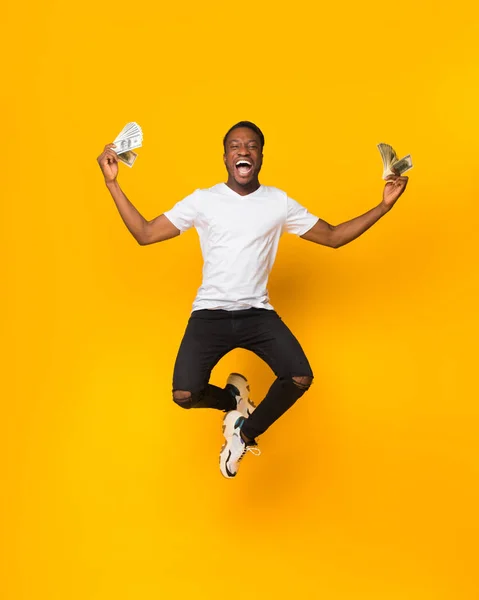 Afro-americano saltando sosteniendo montón de dinero, fondo amarillo —  Fotos de Stock