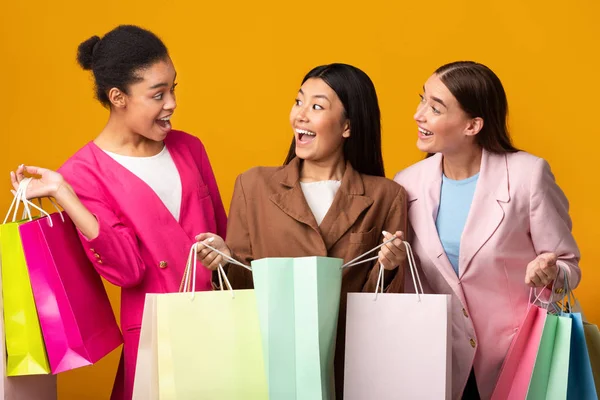 Tres mujeres felices sosteniendo bolsas de compras de pie sobre fondo amarillo — Foto de Stock