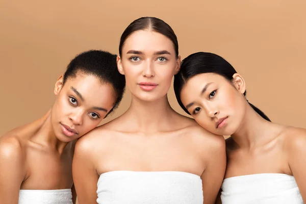 Três meninas embrulhadas em toalhas posando sobre fundo bege — Fotografia de Stock