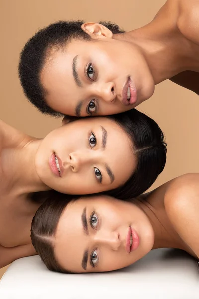Портрет трех привлекательных женщин, смотрящих в камеру, бежевый фон — стоковое фото