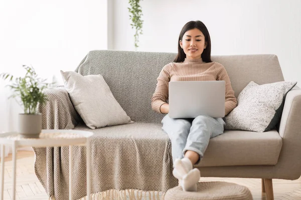 Asiatisk flicka surfa internet på laptop, vilar på soffan — Stockfoto