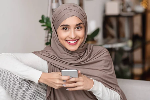 Portrait of happy muslim girl in hijab using smartphone at home — Stok Foto