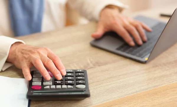 Руки літніх чоловіків використовуючи калькулятор і ноутбук в офісі — стокове фото