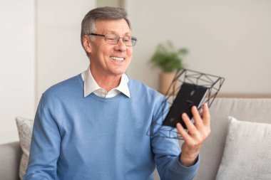 İçerideki koltukta oturan aile resmine bakan yaşlı adam.