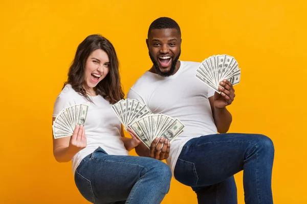 Nadšený multiraciální pár pózující s hromadami dolarové hotovosti v rukou — Stock fotografie