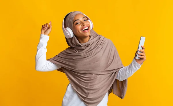 Gadis muslim berkulit hitam ceria dengan smartphone mendengarkan musik di headphone nirkabel — Stok Foto