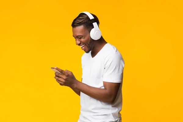 Chico afroamericano en auriculares usando teléfono celular sobre fondo amarillo —  Fotos de Stock