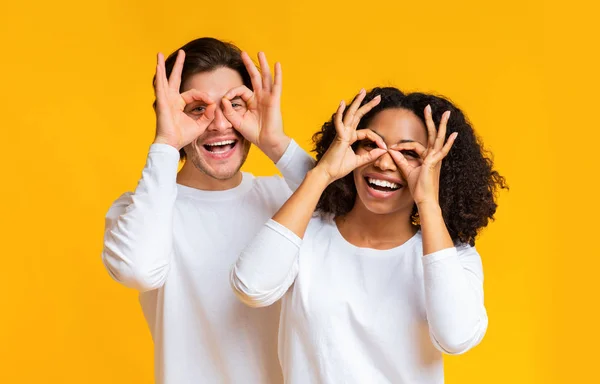Joyful interracial couple fooling together, making funny glasses with fingers — ストック写真