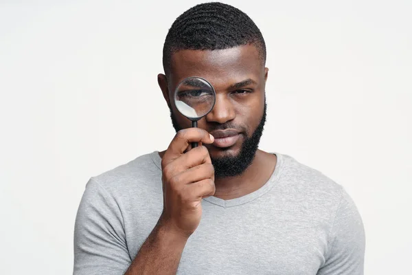 Suspicious young man looking at camera through magnifier — 스톡 사진