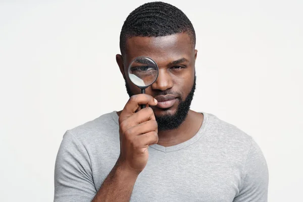 Suspicious young man looking at camera through magnifier — ストック写真