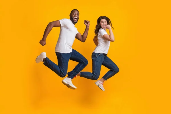 Funny interracial couple jumping and running in the air, yellow background — Stock Photo, Image