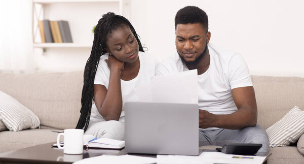 Черная пара управляет семейным бюджетом дома вместе, читает финансовые документы

