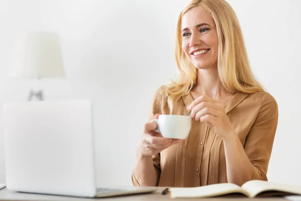 Mujer emprendedora feliz bebiendo café, trabajando en el ordenador portátil — Foto de Stock