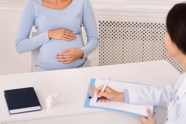 Неузнаваемый доктор делает заметки, слушая беременную женщину во время назначения — стоковое фото