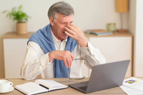 Älterer Geschäftsmann am Laptop massiert Nasenrücken und hat Kopfschmerzen im Büro — Stockfoto