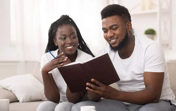 Afro casal olhando para notepad em casa, verificando planos e lista de afazeres — Fotografia de Stock