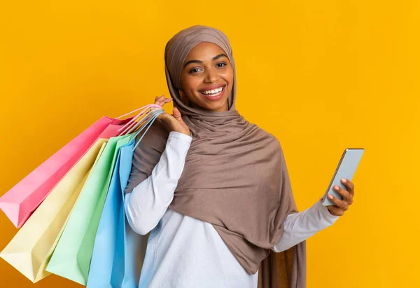 Black muslim girl in headscarf with smartphone and bright shopping bags — Stok fotoğraf