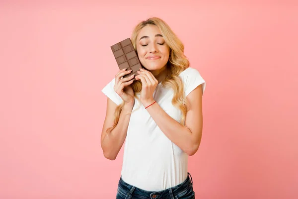 Mulher muito milenar abraçando barra de chocolate, fundo rosa — Fotografia de Stock