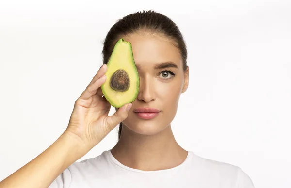 Jonge dame met Avocado half in de buurt gezicht poseren, Studio schot — Stockfoto