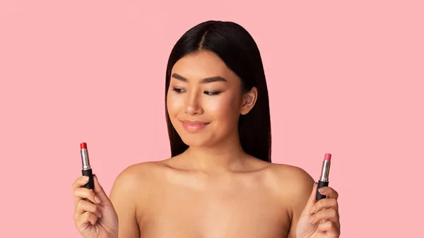 Beauty trends. Asian girl choosing between two lipstick colors — Stok fotoğraf