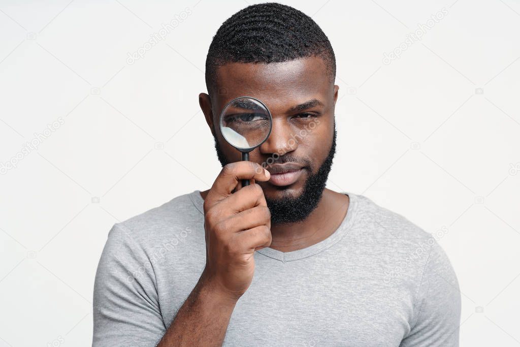 Suspicious young man looking at camera through magnifier