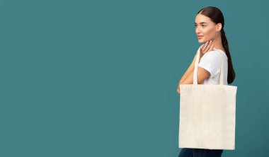 Young Woman Holding White Eco Bag Standing On Turquoise Background