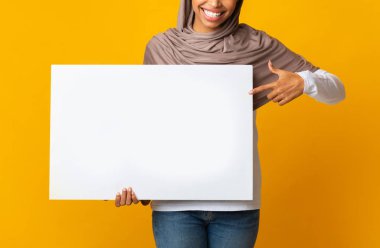 Başörtüsü içinde tanınmayan siyah kız elindeki boş levhaya işaret ediyor.