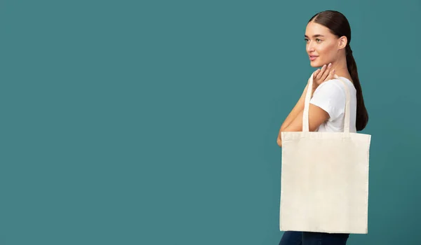 Joven mujer sosteniendo blanco eco bolsa de pie sobre fondo turquesa —  Fotos de Stock