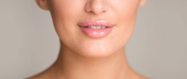 Lip augmentation. Woman with plump lips over gray background