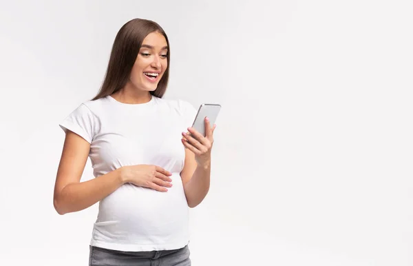 Heureuse femme enceinte utilisant smartphone debout sur fond de studio blanc — Photo