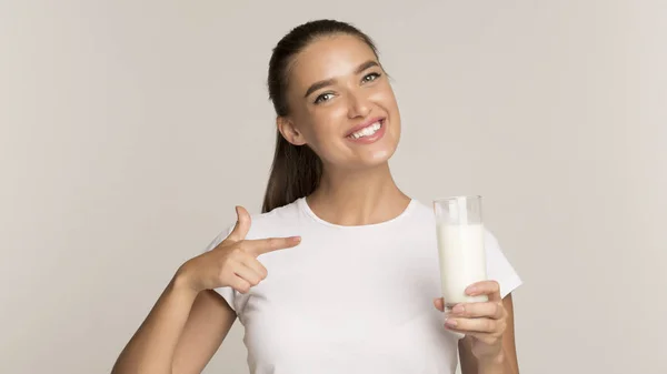 ミルクを持っている若い女性は灰色の背景の上に立って指を指す — ストック写真