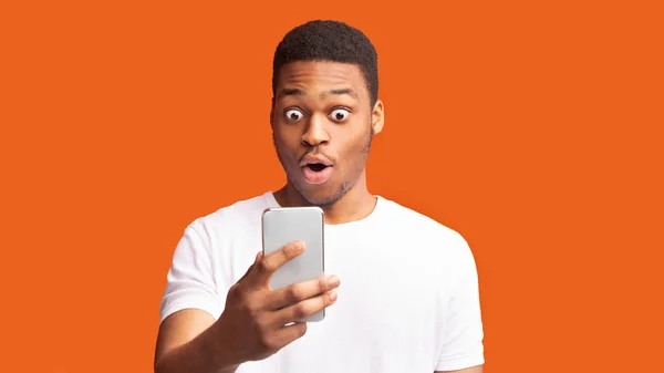 Szoros portré egy meglepett afrikai fickóról, aki a telefont nézi. — Stock Fotó