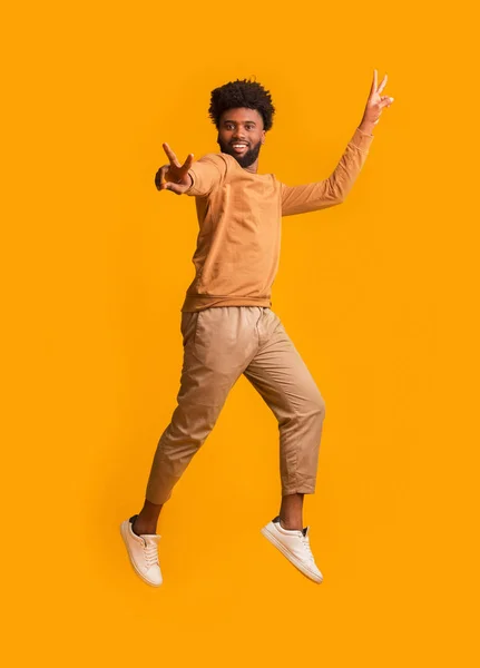 Active black man gesturing peace while jumping in the air — Stock Photo, Image
