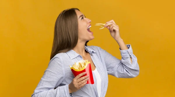 黄色い背景の上に立つフランスのポテトを食べる千年の女の子、パノラマ — ストック写真