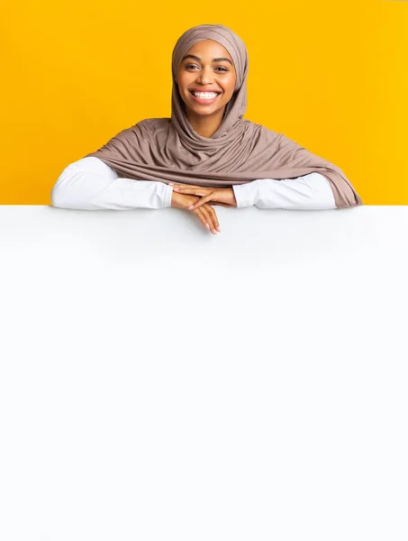 Χαμογελώντας μαύρο μουσουλμάνο κορίτσι με μαντίλα ακουμπά σε λευκό πίνακα διαφήμισης — Φωτογραφία Αρχείου