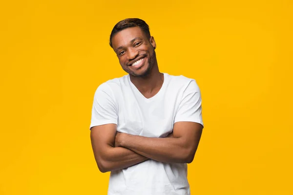 Hombre afroamericano sonriendo cruzando las manos de pie sobre fondo amarillo —  Fotos de Stock