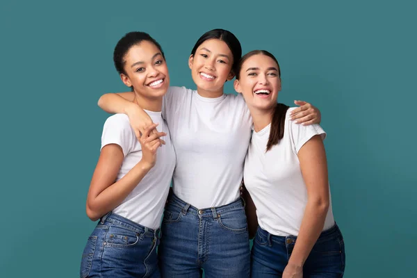 Tres mujeres felices abrazando de pie sobre fondo turquesa, Studio Shot — Foto de Stock