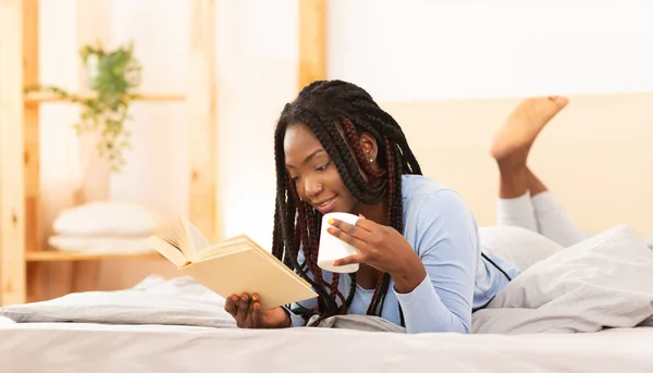 Lady lettura libro avendo caffè sdraiato a letto a casa — Foto Stock