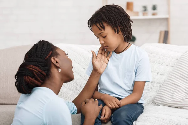 Negro mamá acariciando su deprimido niño en sofá — Foto de Stock