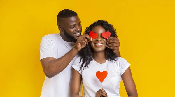 Afro cara cobrindo sua mulher olhos com vermelho valentine cartões — Fotografia de Stock