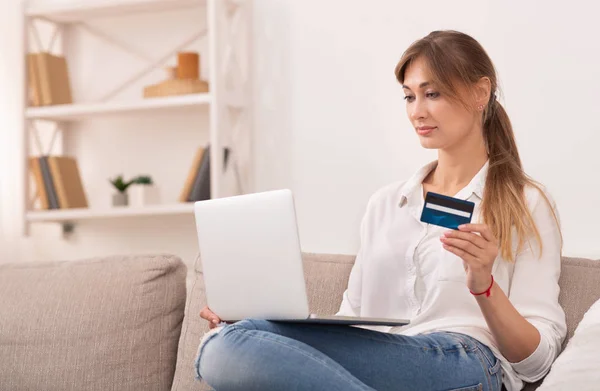 Mujer usando el ordenador portátil que sostiene la tarjeta de crédito Sentado en el sofá interior — Foto de Stock