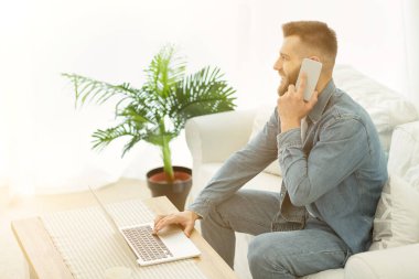 Genç çalışan telefonla konuşuyor, laptopla çalışıyor.