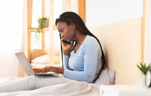 Mulher falando no telefone trabalhando no portátil na cama interior — Fotografia de Stock