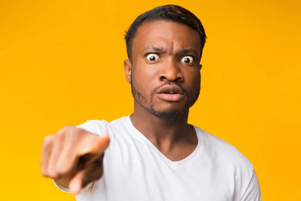 Uomo afroamericano pazzo che punta il dito alla macchina fotografica, sfondo giallo — Foto Stock