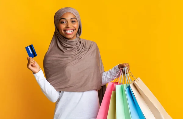 Chica musulmana negra en pañuelo para la cabeza con tarjeta de crédito y bolsas de compras —  Fotos de Stock