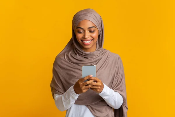 Černá islámská dívka v hidžábu pomocí smartphonu, textových zpráv nebo čtení zpráv — Stock fotografie
